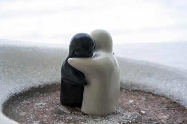 愛は、バレンタインデーの概念氷を溶かします。F 少女と少年人形は、背景をぼかした写真が白い雪の上に立って、お互いを抱擁します。彫刻を抱き締めます。お土産。大理石のオブジェクト。大好きです。共感 - 写真・画像