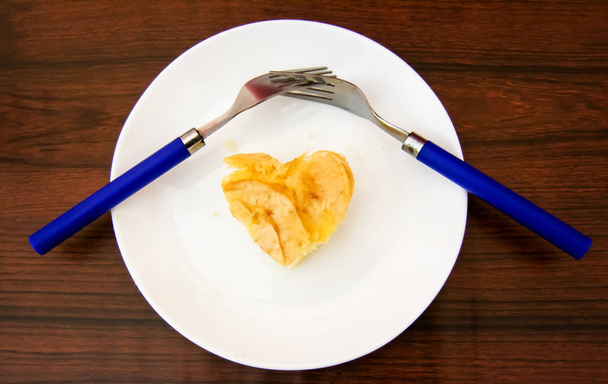 Piece of apple pie with heart shape and two forks interlaced on  - Photo, Image