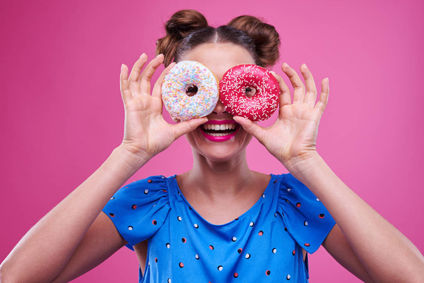 Szczęśliwa młoda dziewczyna zerkające przez dwa posypane donutnuts - Zdjęcie, obraz