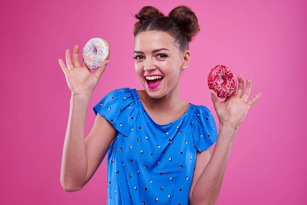 Positive young girl holding two sprinkled doughnuts - Photo, Image