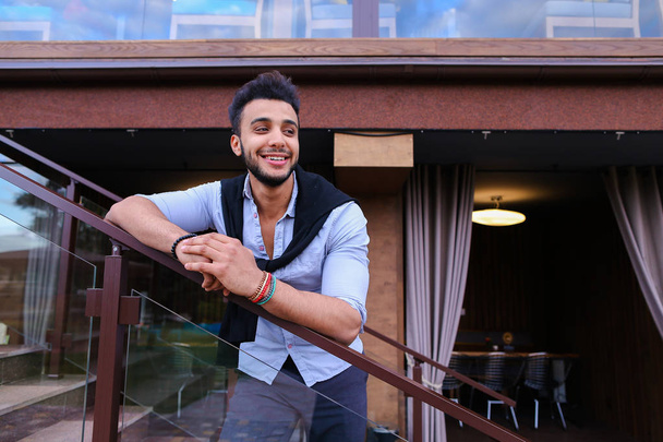 Nuori hymyilevä komea mies arabi ulkonäkö nojaa rintojen ha
 - Valokuva, kuva