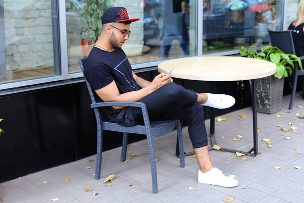 Yksi nuori komea arabialainen mies käyttää puhelinta, istuu juttelemassa ja istuu
 - Valokuva, kuva