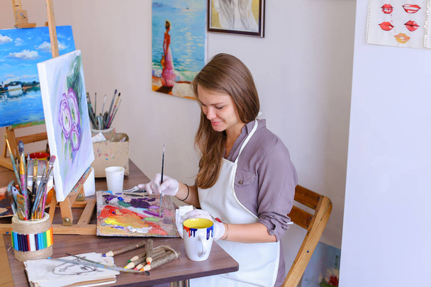 Mädchen sitzt auf Hocker an Staffelei und schreibt Malerei, benutzt Pinsel, um - Foto, Bild