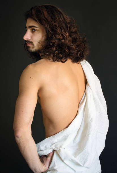Φωτογραφία: όμορφος άντρας με μακριά σγουρά μαλλιά με λευκή υφασματεμποριών είναι πίσω - Φωτογραφία, εικόνα