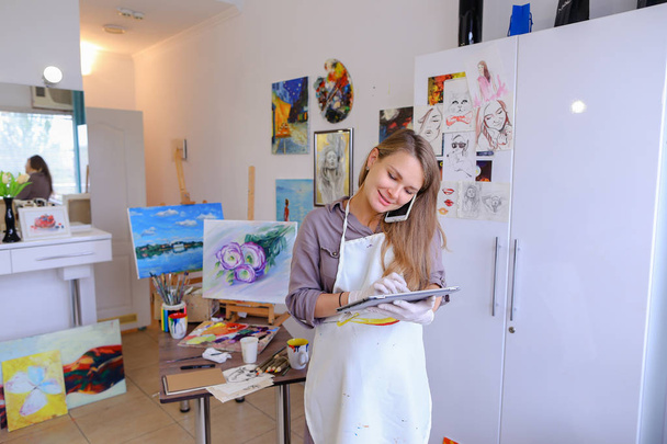 Девушка художник держит мобильный телефон и использовать, говорить, писать ручку о
 - Фото, изображение