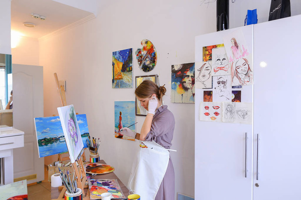 Beautiful young painter paints picture uses brushes and oil, and - Photo, Image