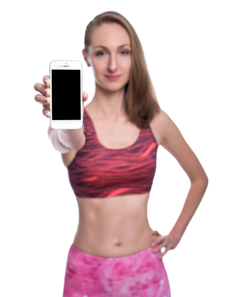 Happy smiling fitness girl showing blank smartphone screen in studio. Isolated over white background. - Valokuva, kuva