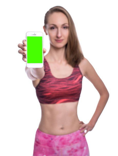 Happy smiling fitness girl showing chromakey smartphone screen in studio. Isolated over white background. - 写真・画像