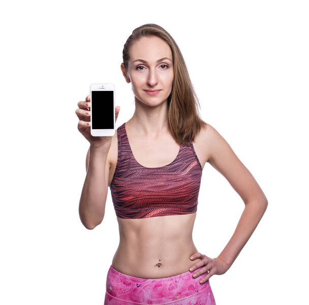 Happy smiling fitness girl showing blank smartphone screen in studio. Isolated over white background. - Zdjęcie, obraz
