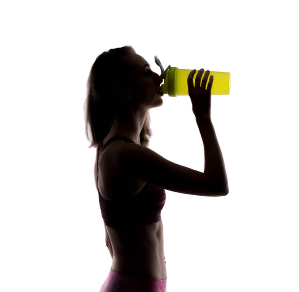 fröhliche sportliche Frau, die im Studio aus einer grünen Shake-Flasche trinkt. Silhouettenfoto. isoliert auf weißem Hintergrund. - Foto, Bild