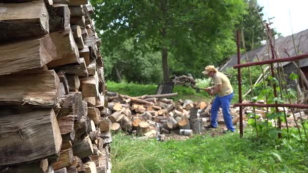 gestapeltes Brennholz und verschwommener Bauer, der im Hinterhof Holz hackt. 4k - Filmmaterial, Video