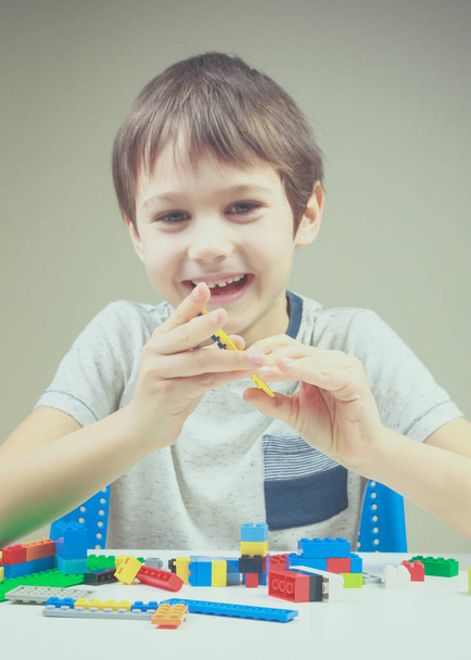 Niño sonriente jugando con ladrillos de construcción de plástico de colores en casa
 - Foto, Imagen