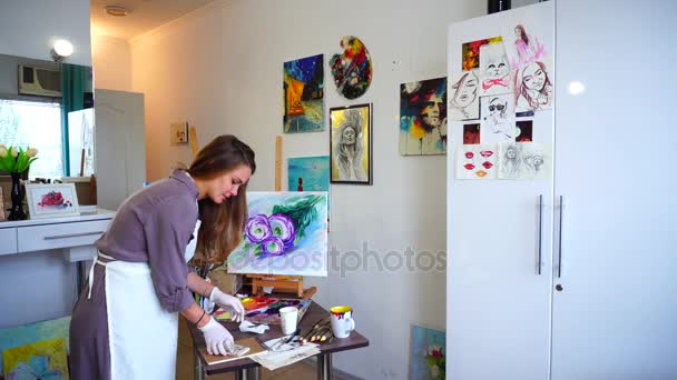 Χαριτωμένο μικρό κορίτσι ζωγράφος χρώματα εικόνα και να απαντήσετε σε εισερχόμενη κλήση από το Smartphone, σε διάλογο και να γράφει στο σημειωματάριό χειρίζονται το λευκό στούντιο τέχνης. - Πλάνα, βίντεο