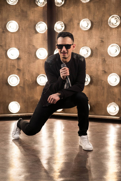Mężczyzna wokalistka w okulary śpiewa na scenie w rzutniki światła - Zdjęcie, obraz