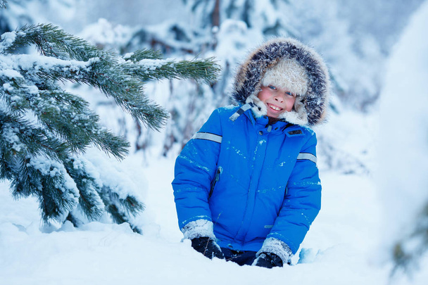 Cute little boy wearing warm clothes playing on winter forest - Fotoğraf, Görsel