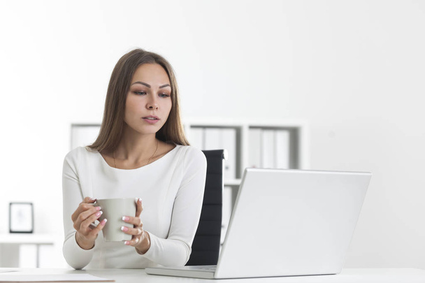 Pensive girl with coffee in white office - Photo, image