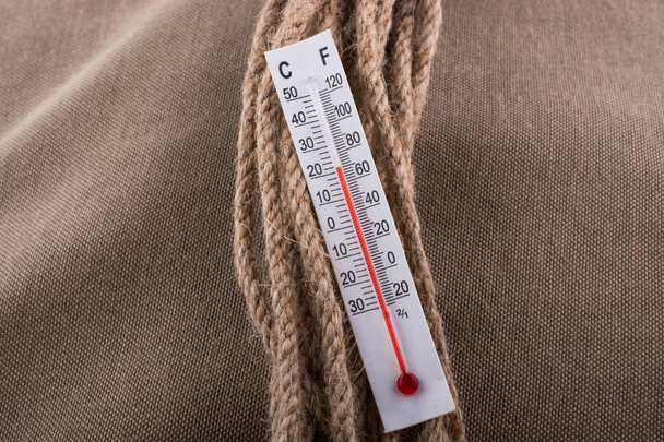 Lämpömittari ruskealla köydellä kankaan taustalla
  - Valokuva, kuva