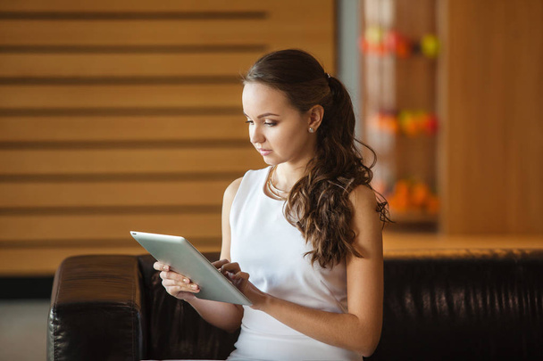 Pretty girl sitting on leather sofa and holding tablet - Photo, Image
