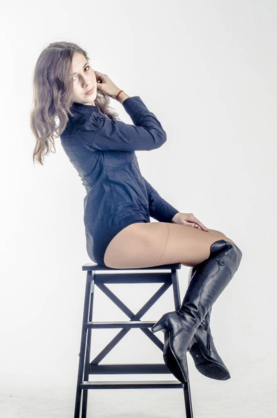  Young girl with curly hair sits gracefully coquettish in a dark shirt and high boots with heels - Fotoğraf, Görsel