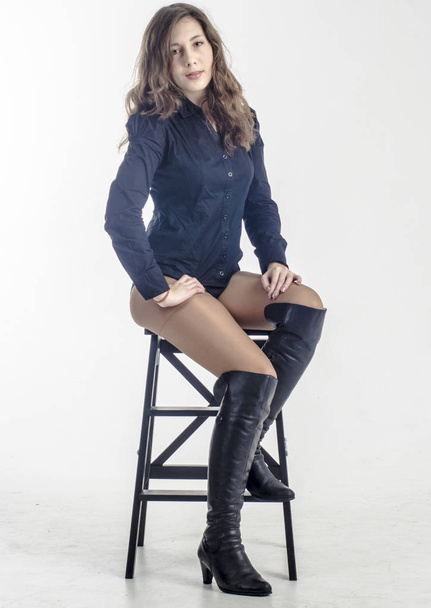  Young girl with curly hair sits gracefully coquettish in a dark shirt and high boots with heels - Foto, imagen