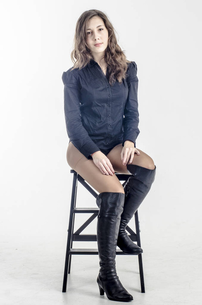  Young girl with curly hair sits gracefully coquettish in a dark shirt and high boots with heels - Fotó, kép