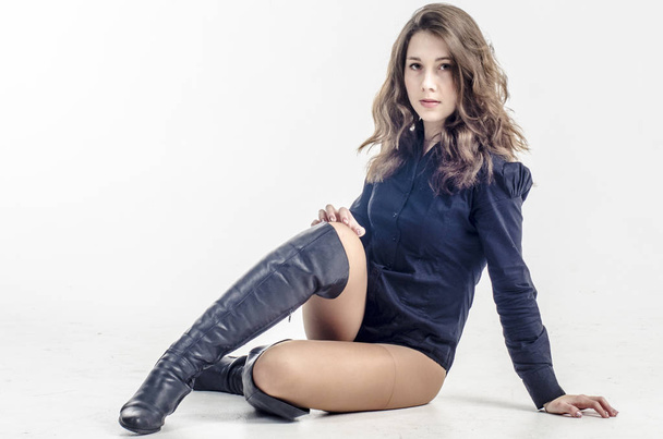  Young girl with curly hair sits gracefully coquettish in a dark shirt and high boots with heels - Fotó, kép