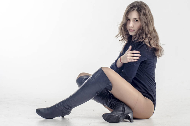  Chica joven con el pelo rizado se sienta elegantemente coqueta en una camisa oscura y botas altas con tacones
 - Foto, imagen
