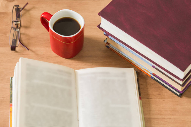 Stapel geschlossener Bücher und geöffnetes Buch mit Tasse Kaffee - Foto, Bild