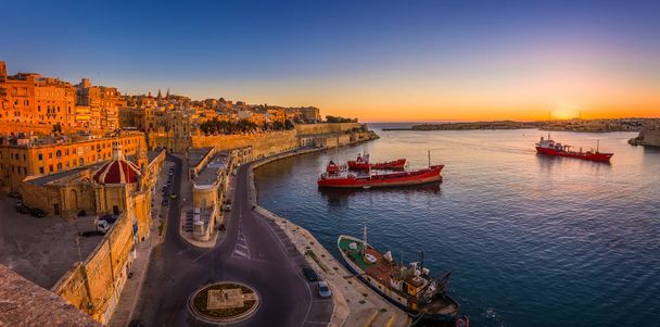 Βαλέτα, Μάλτα - πανοραμικό στιγμιότυπο από μια καταπληκτική ανατολή του ηλίου το καλοκαίρι στο λιμάνι Grand της Βαλέτα με πλοία και τα αρχαία σπίτια και τους τοίχους της Μάλτας πρωτεύουσας. - Φωτογραφία, εικόνα