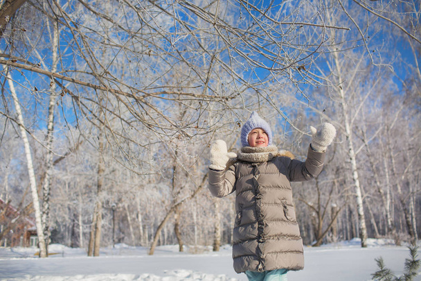 Little girl in grey jacket walks in winter park in sunny day - Foto, immagini