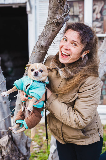 Portrait of young attractive laughing woman holding Chihuahua dog outdoors - Photo, Image