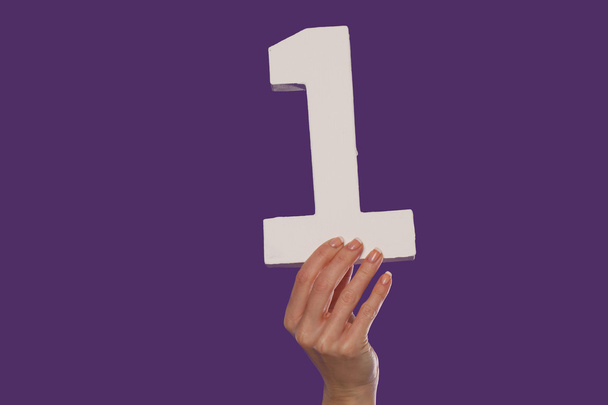 weibliche Hand hält die Zahl 1 von unten hoch - Foto, Bild