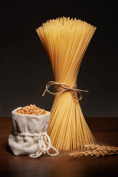 Dry spaghetti pasta, burlap bag of grains and wheat ears  - Photo, Image