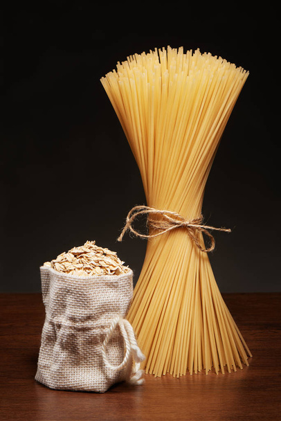 Dry spaghetti pasta and burlap bag of oatmeal on table  - Fotó, kép