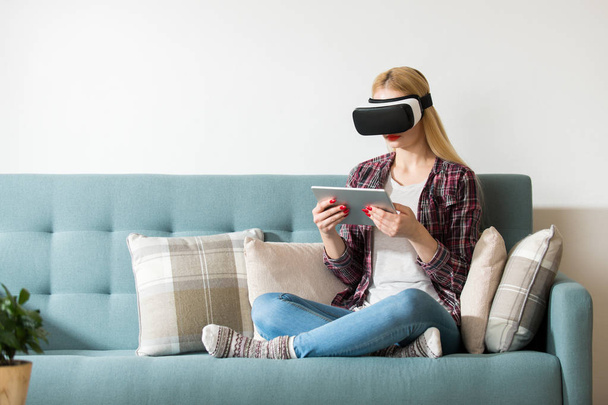 Atrakcyjna kobieta nosi okulary wirtualnej rzeczywistości, leżąc na kanapie. Zestaw wirtualnej rzeczywistości. Koncepcja wirtualnej rzeczywistości życia. - Zdjęcie, obraz