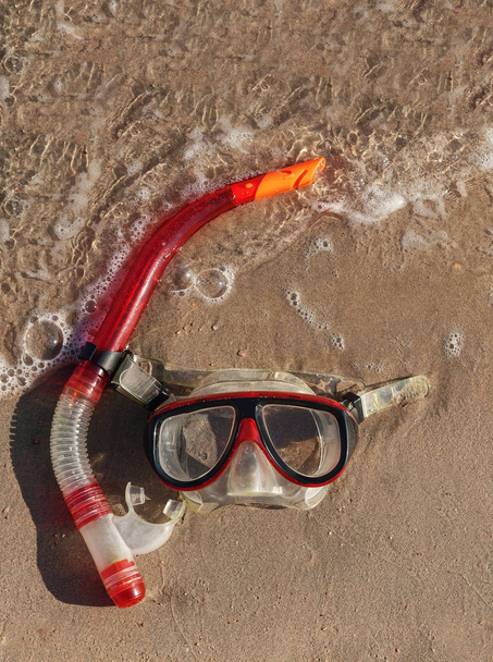 masker en snorkel liggend op nat zand met golven - Foto, afbeelding