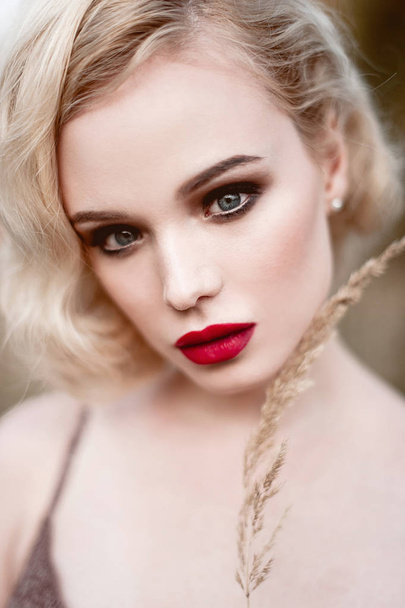Beautiful and elegant smiling sexy blonde woman with red lips and hair waves wearing beige liingerie posing on the field outdoors summer, retro vintage style and fashion. Retouched close up face fine  - 写真・画像
