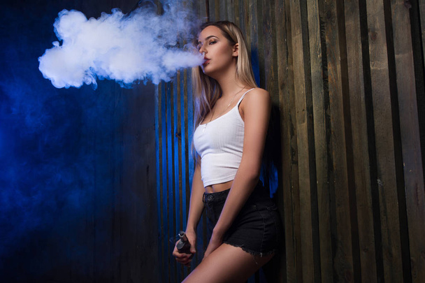 Nube de humo. Sexy chica vapeando y fumando cigarrillo electrónico
. - Foto, Imagen