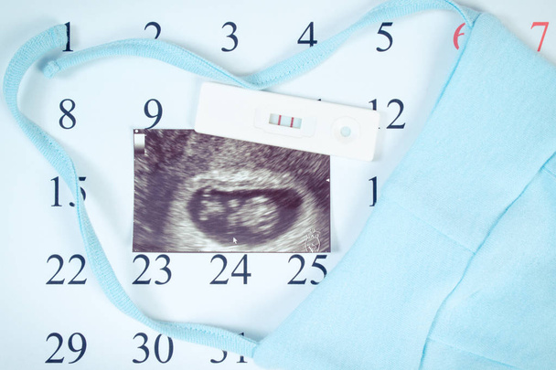 Teste de gravidez, ultra-som do bebê e roupas para recém-nascido no calendário, esperando para o bebê
 - Foto, Imagem