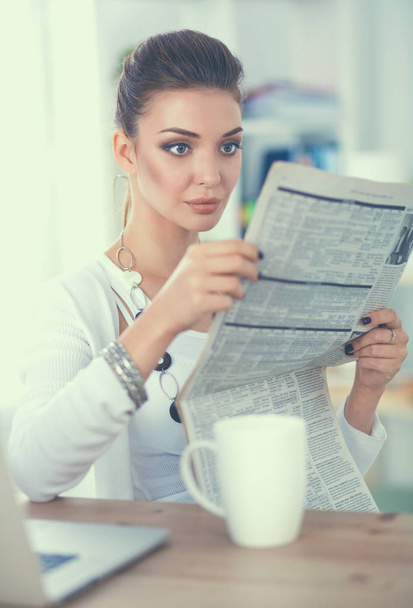 Cute businesswoman holding newspaper sitting at her desk in bright office - Zdjęcie, obraz