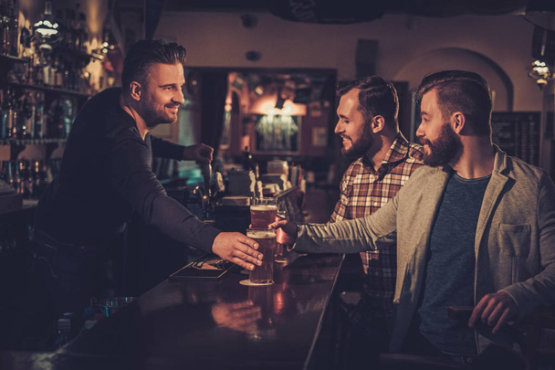 Cheerful old friends drinking draft beer at bar counter in pub. - Фото, зображення