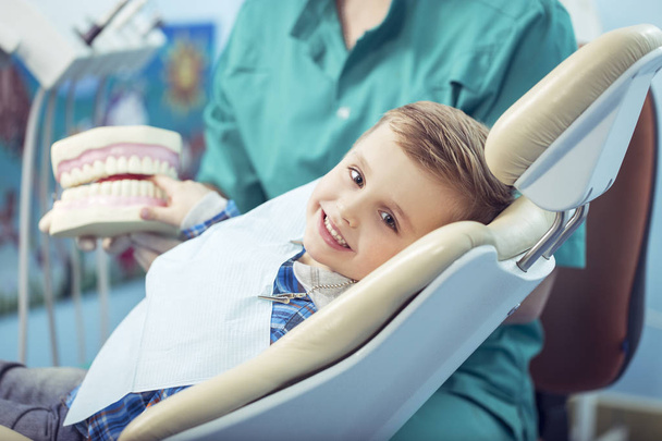 πολύ χαρούμενος αγόρι αφού ο γιατρός στην κλινική, κρατώντας ένα σαγόνι οδοντιατρική μέσα της τα χέρια και να έχουν ένα όμορφα λευκά χαμόγελα. Αντίγραφο χώρου - Φωτογραφία, εικόνα