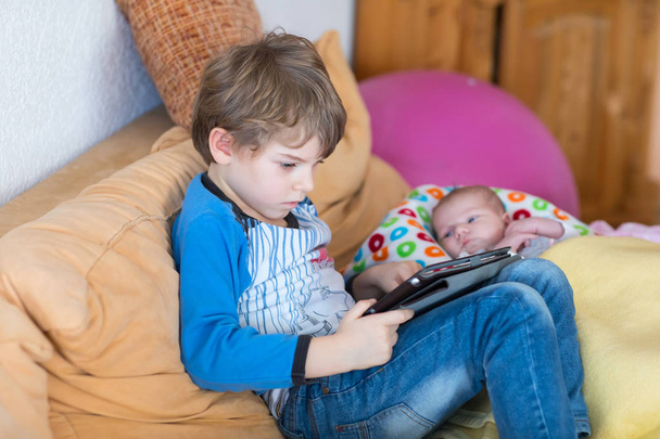 Chłopiec dzieci w wieku przedszkolnym dziecko grając w gry tablet komputer. Cute noworodka, patrząc na brata. - Zdjęcie, obraz