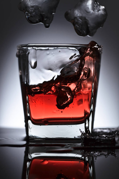Lasi viskiä putoavalla jäällä mustalla pohjalla
 - Valokuva, kuva