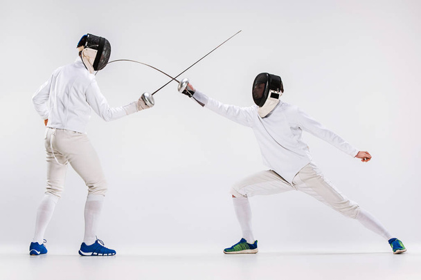The two men wearing fencing suit practicing with sword against gray - Foto, Imagen