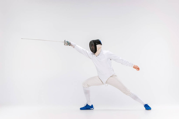 Man wearing fencing suit practicing with sword against gray - Foto, Imagem