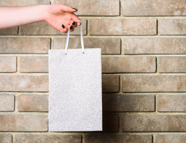 white shopping bag in female hand on brick wall - Foto, imagen