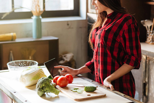 Cropped image of woman standing in kitchen with tablet computer - Foto, immagini