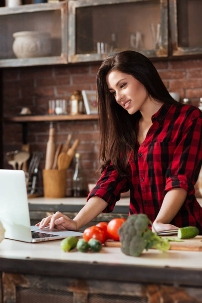 Vertical image of woman standing in kitchen with laptop - Photo, image