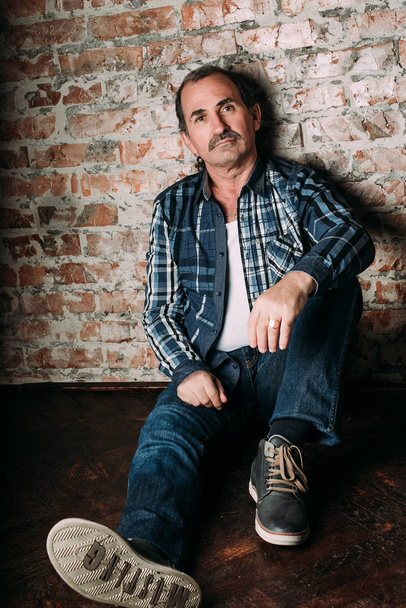 Handsome middle aged man is dressed in a casual clothing. Red brick wall background. - Photo, Image